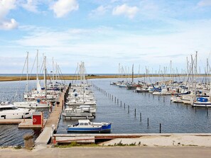 A marina with multiple boats docked, a wooden walkway, and a clear sky.