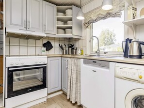 A kitchen with white cabinets, a stove, a dishwasher, and a window with curtains. - 7 Person Holiday Home in Hals (Hals)