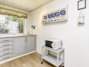 A kitchen with a microwave on a cart, a window with a view, and a shelf with blue and white plates. - 7 Person Holiday Home in Hals (Hals)