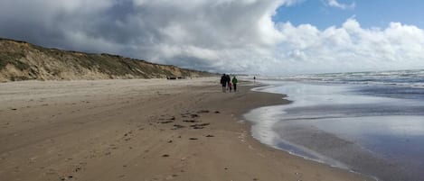 A sandy beach with footprints, a cliff, and a cloudy sky.