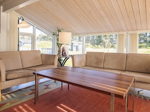 A room with a wooden table, two beige sofas, a patterned rug, and a lamp.