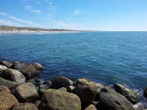 A rocky shoreline with calm sea water, a distant beach, and a clear sky. - 5 Star Holiday Home in Lokken (Lokken)