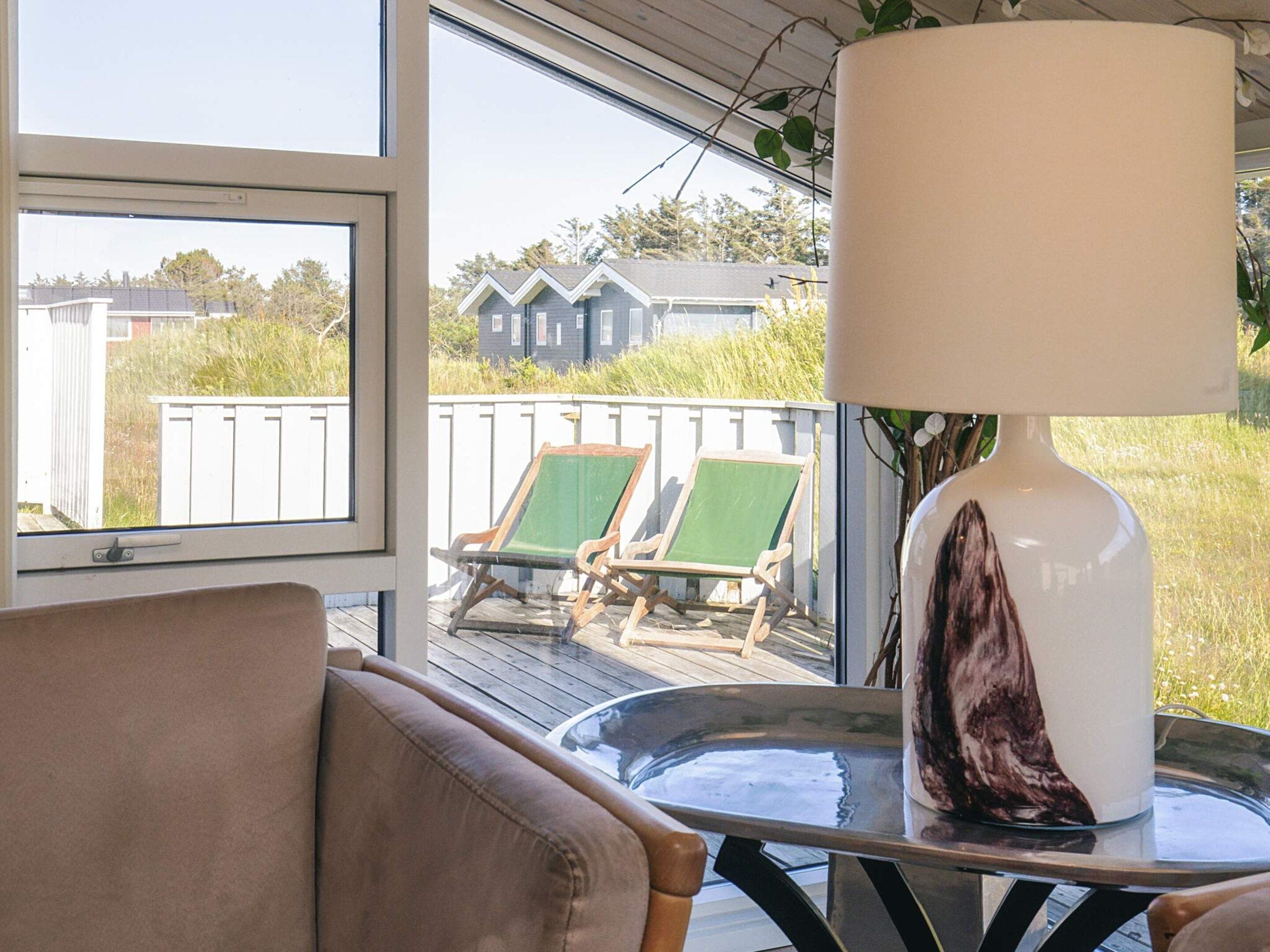 Ein Zimmer mit Blick auf eine Terrasse, zwei grüne Stühle, eine weiße Lampe und ein Glastisch.