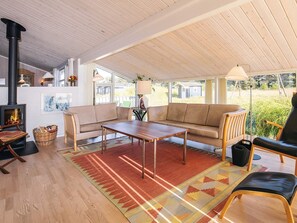 A cozy living room with a fireplace, sofa, coffee table, and large windows.