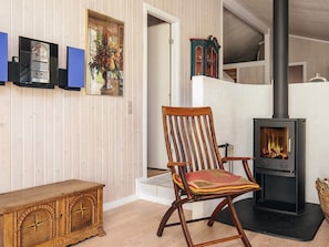 A wooden rocking chair with a cushion, a black wood-burning stove, and a wooden cabinet with a star design. - 5 Star Holiday Home in Lokken (Lokken)