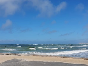 Una platja amb onades, cel blau i una passarel·la de fusta.