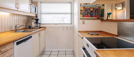 A compact kitchen with a dishwasher, stove, and a window with blinds.