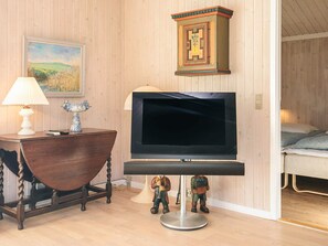 A room with a wooden floor, a television on a stand, a lamp, a small table, and a painting on the wall. - 5 Star Holiday Home in Lokken (Lokken)