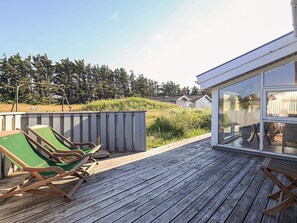 A wooden deck with two green lounge chairs, a wooden swing set, and a view of a residential area with houses and trees.