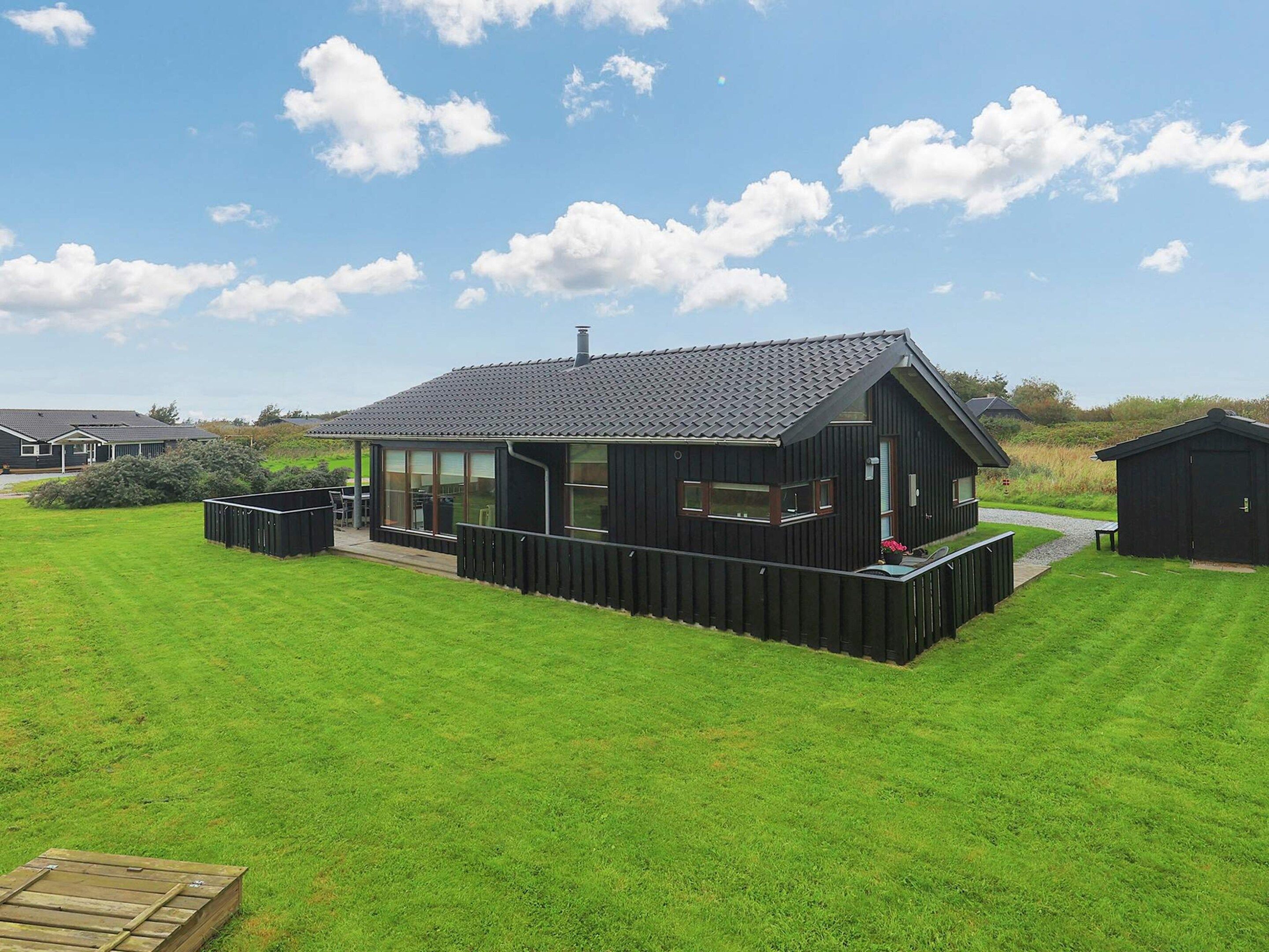 Et moderne hus med en overdækket terrasse, omgivet af en velplejet græsplæne.