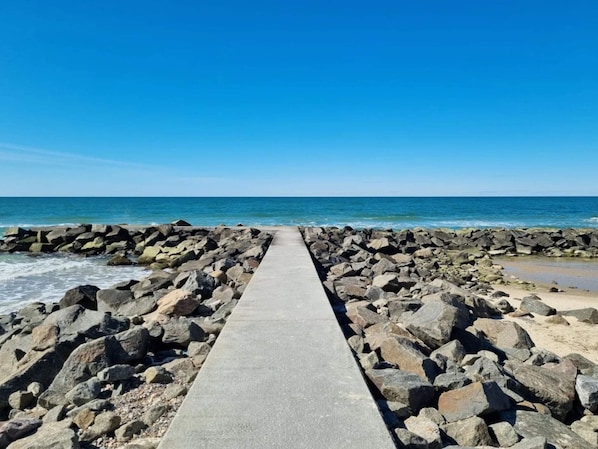 A concrete pathway leading to a rocky shoreline with the ocean in the background.