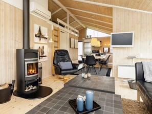 A cozy interior with a wood-burning stove, a leather chair, a dining area, and a TV mounted on the wall.
