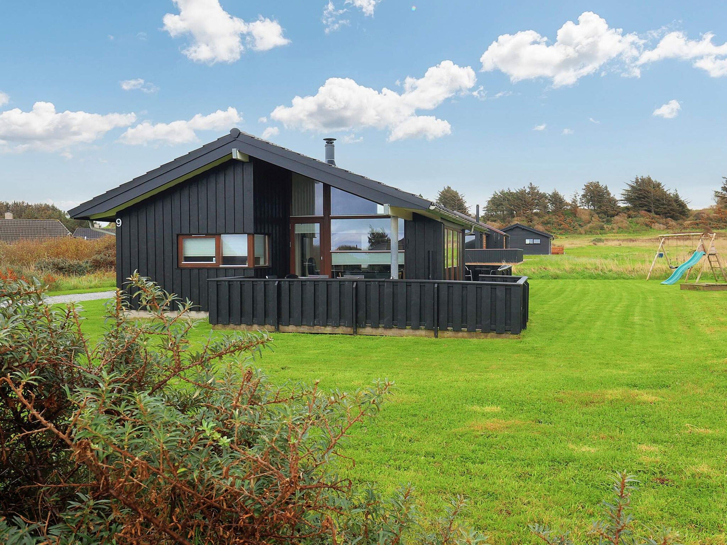 Et moderne hus med en stor terrasse, gyngestativ og græsplæne.