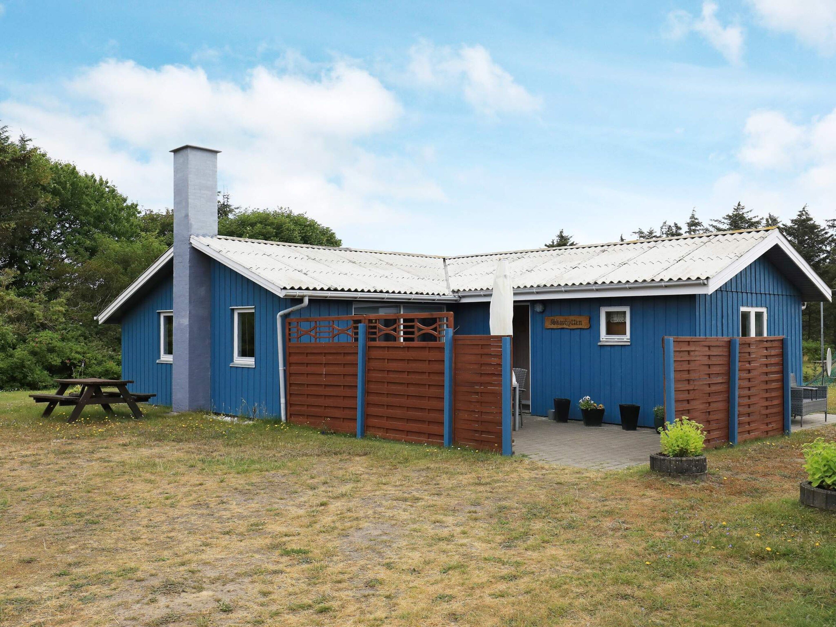 A blue building with a wooden gate, a picnic table, and potted plants.
