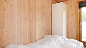 A bedroom with wooden walls, a bed with white bedding, and a door leading outside. - 6 Person Holiday Home in Lokken (Lokken)