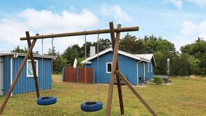 A swing set with two tire swings in a grassy field with a blue building in the background. - 6 Person Holiday Home in Lokken (Lokken)