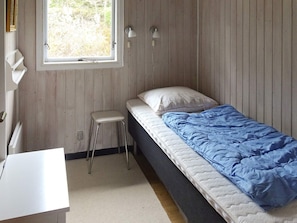 A single-bed room with a window, a small stool, and a desk.