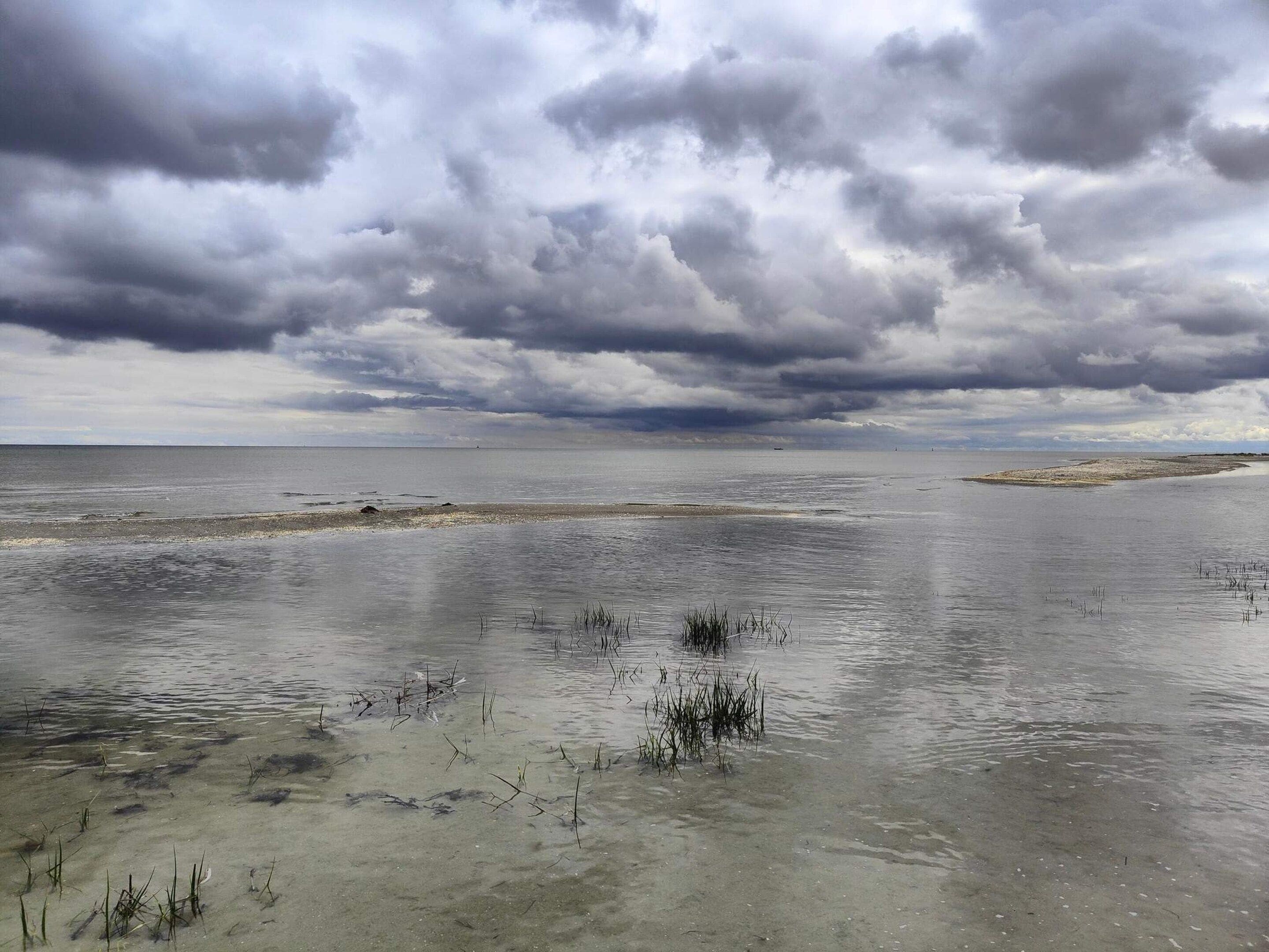 A coastal landscape with a wide expanse of water, a sandy beach, and overcast skies.