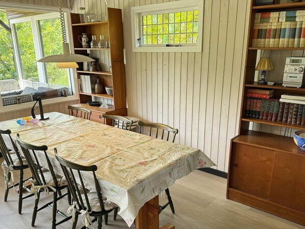 A cozy room with a dining table, chairs, a bookshelf, and a window with a view of greenery.