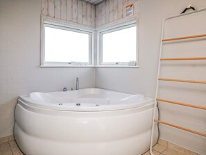 A bathroom with a large bathtub, two windows, and a towel rack. - 5 Star Holiday Home in Hjorring (Hjørring)
