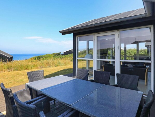 A patio with a table and chairs, a glass enclosure, and a view of the sea.