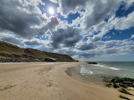 Una playa con costa rocosa, cielos despejados y el sol brillando.