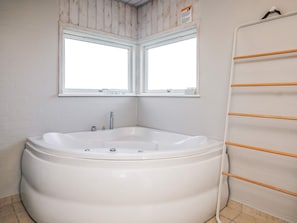 A bathroom with a large bathtub, two windows, and a towel rack. - 5 Star Holiday Home in Hjorring (Hjørring)