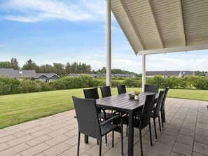 An outdoor patio with a table and chairs, surrounded by a hedge and a view of houses. - 5 Star Holiday Home in Spottrup (Spøttrup)