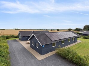 A modern house with a sloped roof and solar panels, surrounded by a well-maintained lawn and fields. - 5 Star Holiday Home in Spottrup (Spøttrup)