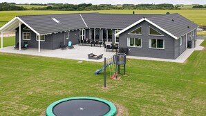 Ein modernes Gebäude mit überdachter Terrasse, einer Schaukel und einem Trampolin.