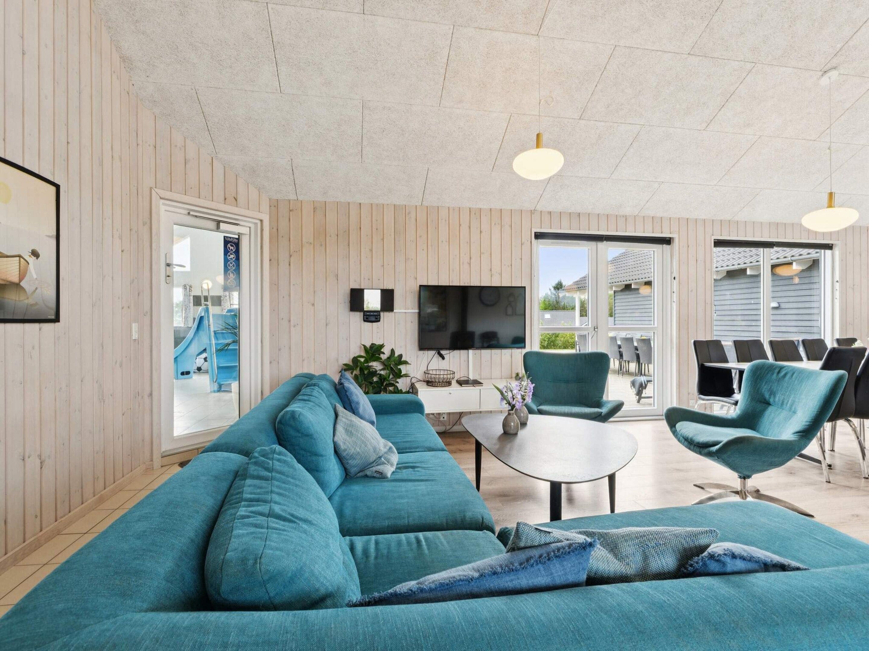 A modern living room with a teal sofa, a coffee table, and a TV mounted on the wall.