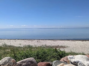 A beach with calm water, a distant sailboat, and a rocky foreground. - 5 Person Holiday Home in Jaegerspris (Jægerspris)