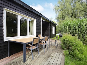 A wooden deck with a table and chairs, a barbecue grill, and a garden area with tall grass and bushes. - 5 Person Holiday Home in Jaegerspris (Jægerspris)
