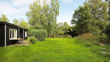 A black cabin with a deck and outdoor seating, surrounded by lush greenery and trees.