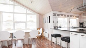 A modern kitchen with a wooden floor, white cabinetry, a bar area, and large windows.