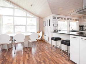 A modern kitchen with a wooden floor, white cabinetry, a bar area, and large windows.