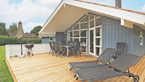 A modern house with a wooden deck, outdoor furniture, and a barbecue grill.