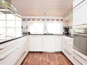 A modern kitchen with white cabinets, a stainless steel range hood, and a wooden floor.