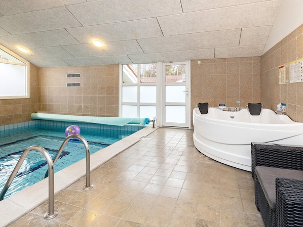 An indoor swimming pool with a jacuzzi, tiled walls, and a clear glass door leading outside.