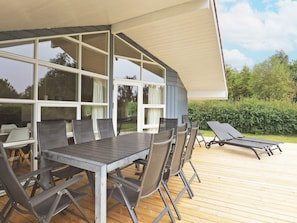 An outdoor patio with a table and chairs, a sun lounger, and a view of the surrounding greenery.