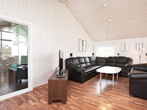 A modern living room with a black leather sofa, a wooden coffee table, and a television on a stand.