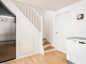 A kitchen with a stainless steel refrigerator, a wooden staircase, and a white door.
