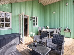 A covered patio with wicker furniture, a glass table, and a barbecue grill.