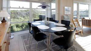 A dining area with a round table, black chairs, and a view of greenery outside. - 4 Star Holiday Home in Lokken (Lokken)