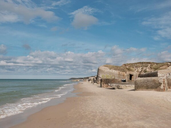 A beach with large concrete structures, a sandy shore, and a calm sea under a partly cloudy sky.