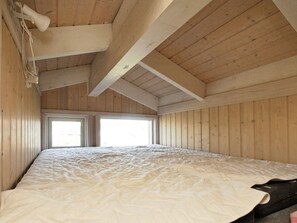 A room with wooden walls and ceiling, a bed with a white mattress, and two windows allowing natural light.