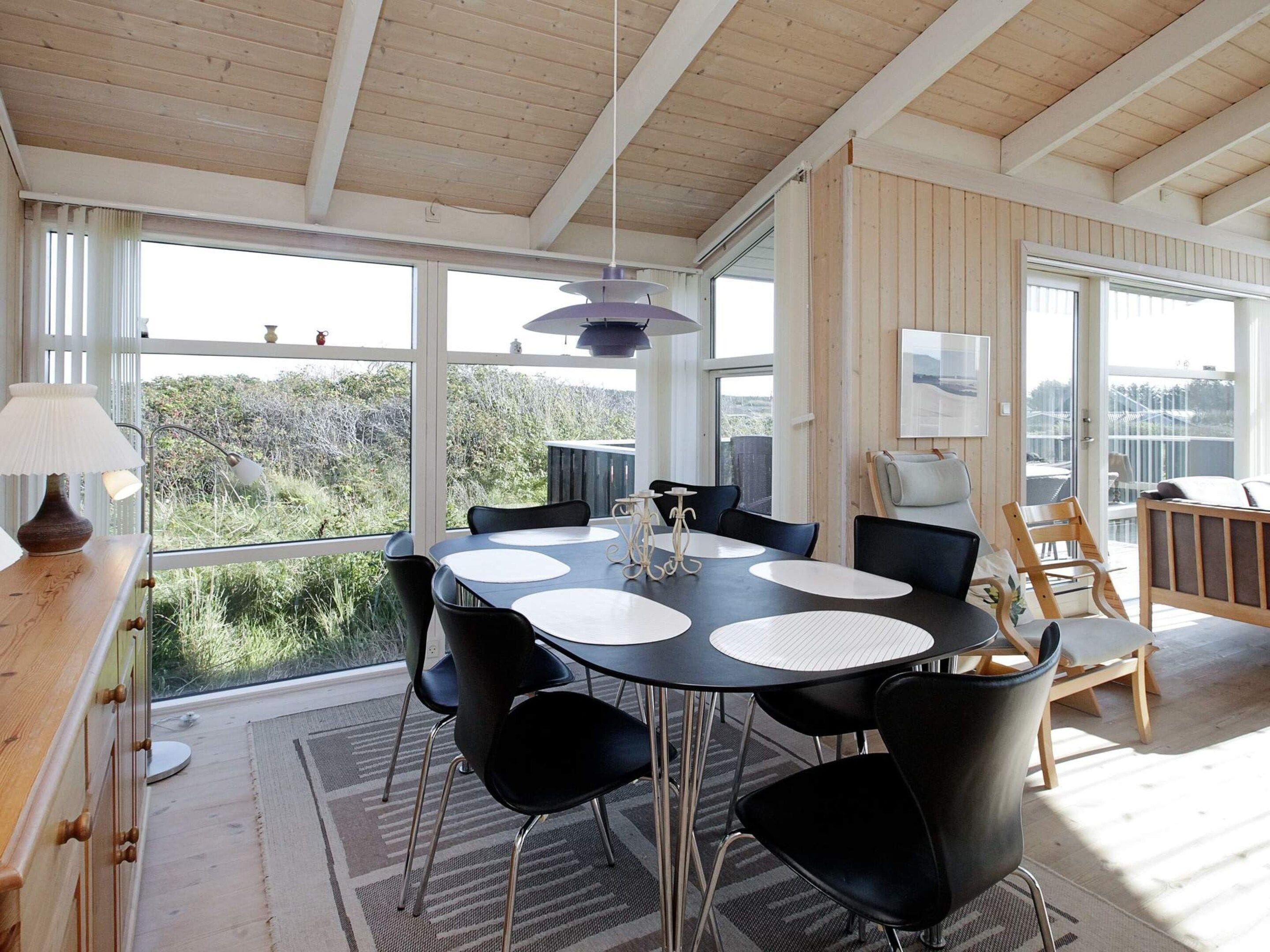 A dining area with a round table, chairs, and a view through large windows.