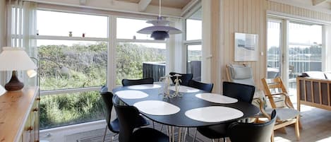 A dining area with a round table, chairs, and a view through large windows.