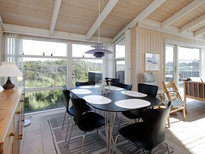 A dining area with a round table, chairs, and a view through large windows.