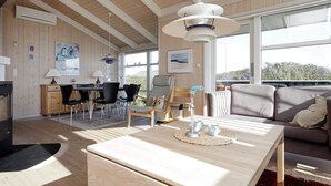 A spacious living area with a wooden ceiling, a dining table with chairs, a sofa, and a large window offering a view of the outdoors. - 4 Star Holiday Home in Lokken (Lokken)